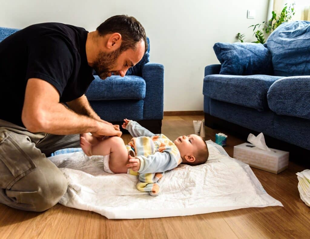 A father is on the floor changing a baby's diaper  - overwhelmed moms.