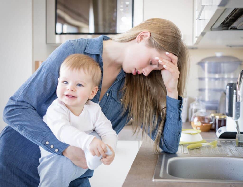 Mom is holding a baby and  looks sick and is bent over a sink about to throw up  - overwhelmed moms.
