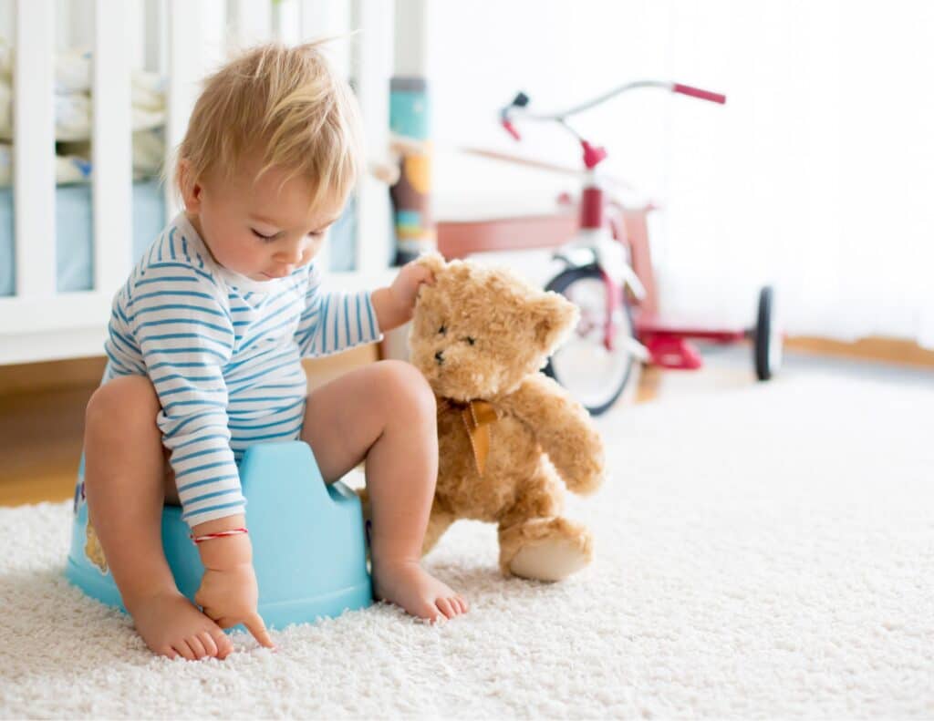 a little child is sitting on a potty holding a toy bear by the ear