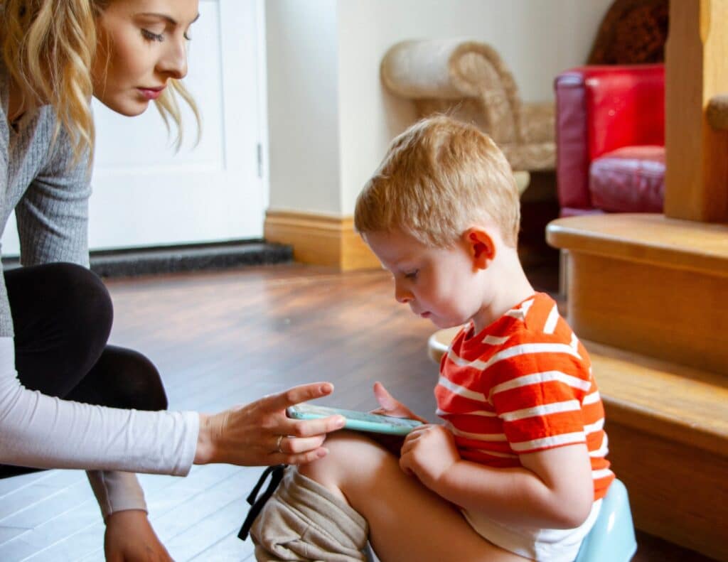 a mother is playing on a phone with her little boy while he sits on a potty - weekend potty training