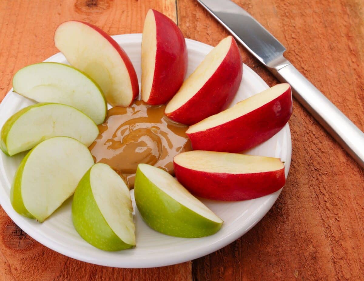 Sliced apples with peanut butter on a plate - cheapest food to buy.