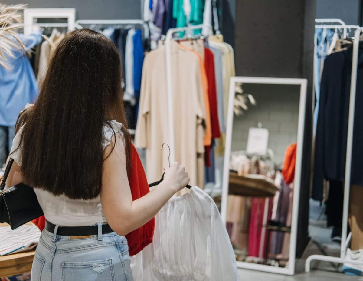 A woman is at a second-hand store looking at a shirt -living frugally on one income.