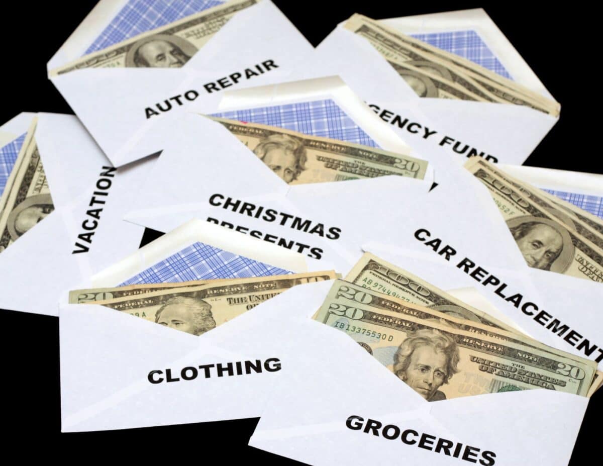 Envelopes with money sticking out with words written on them, "auto repair, vacation, Christmas presents, emergency fund, car replacement, groceries, clothes" -living frugally on one income.