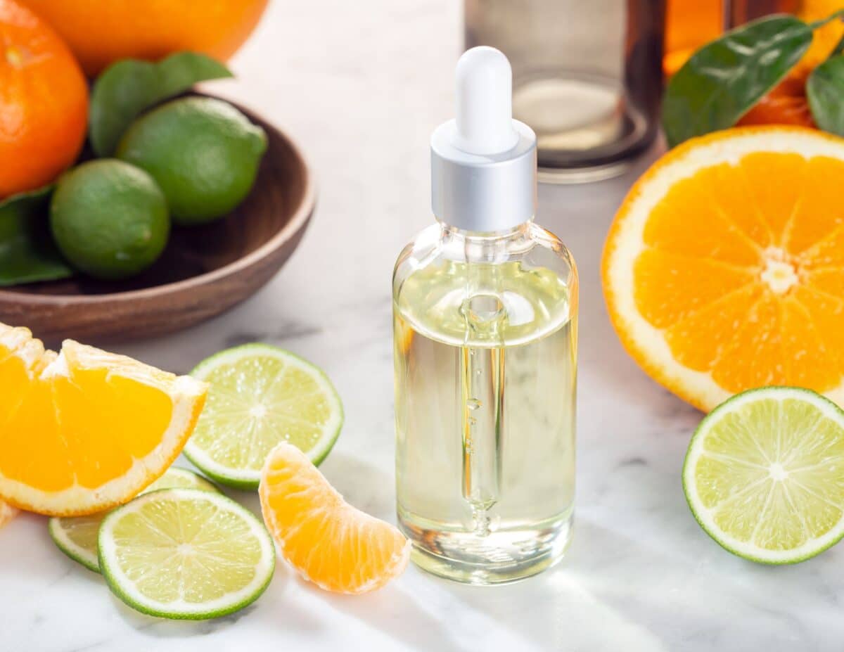 a bottle of essential oil with oranges and limes next to it.