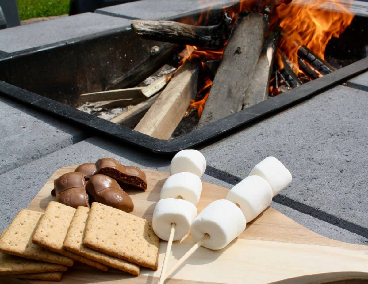 Ingredients for s'mores: marshmallows on sticks, graham crackers, and chocolate by a fire - backyard staycation.