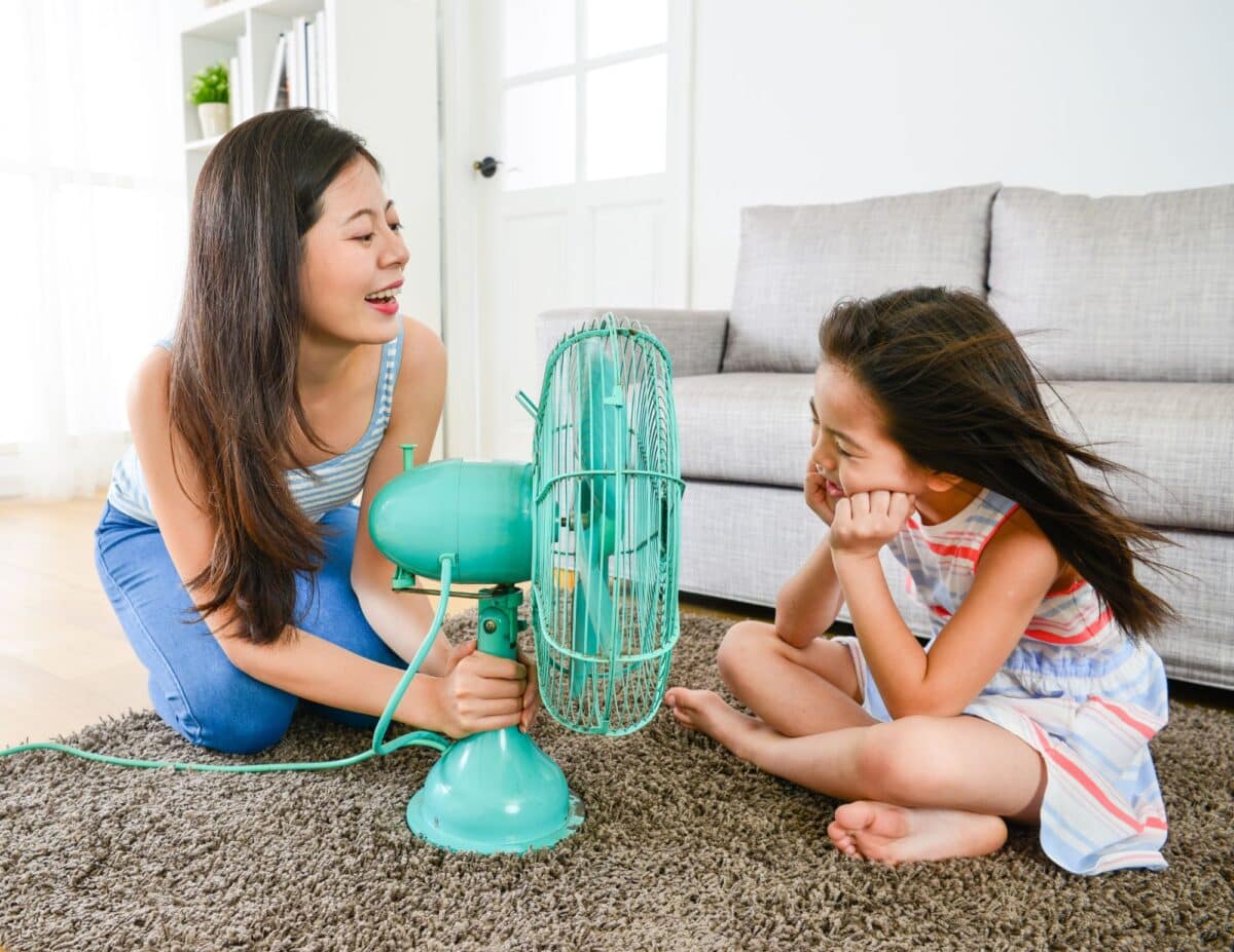 A mother is using a fan to cool off her daughter - how to save money on electric bills in summer.
