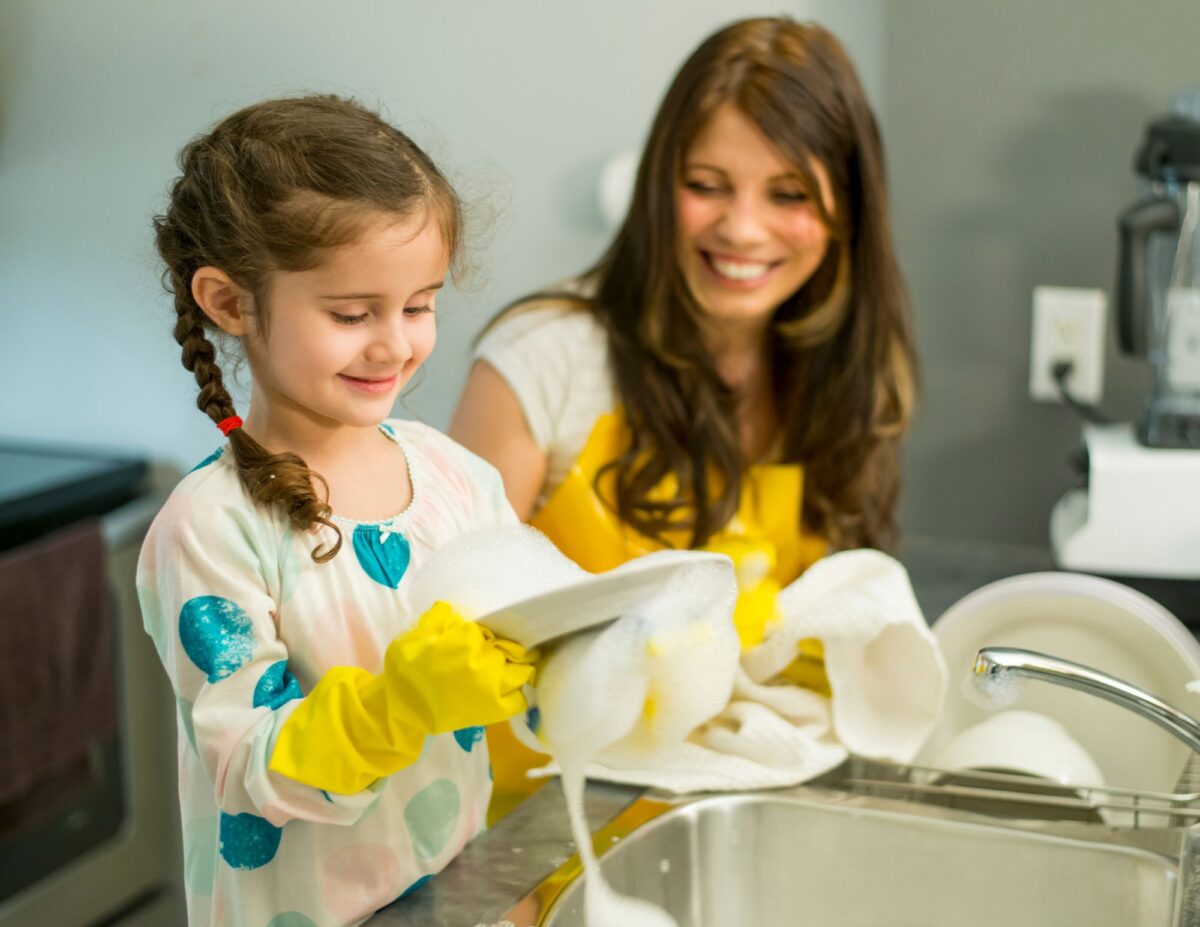 A girl doing dishes while her mother is watching-chores for 8-year-olds.