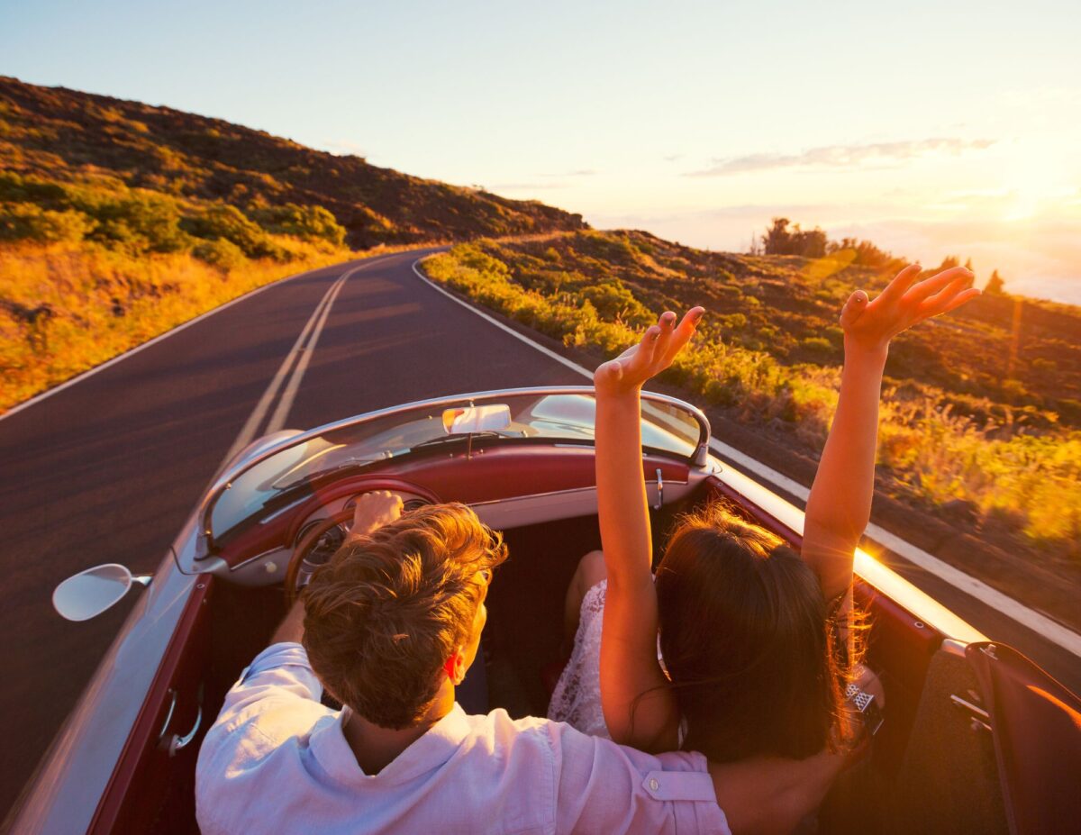 A man and woman are in a convertible on a drive and the woman has her hands in the air - free date ideas.