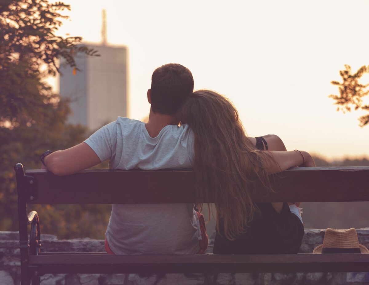 a man and woman are cuddled on a bench looking in the distance - free date ideas.