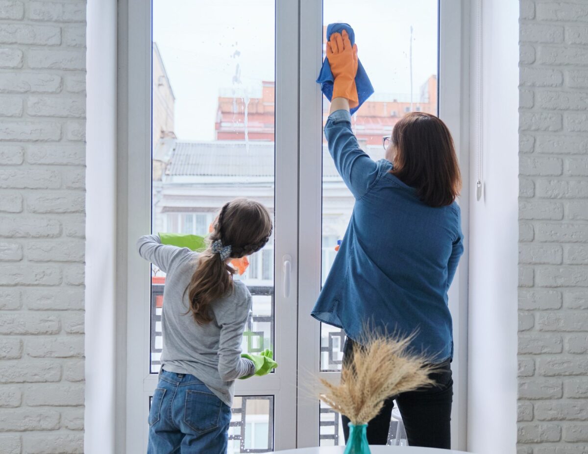A mother is washing a window while her daughter is watching-chores for 8-year-olds.