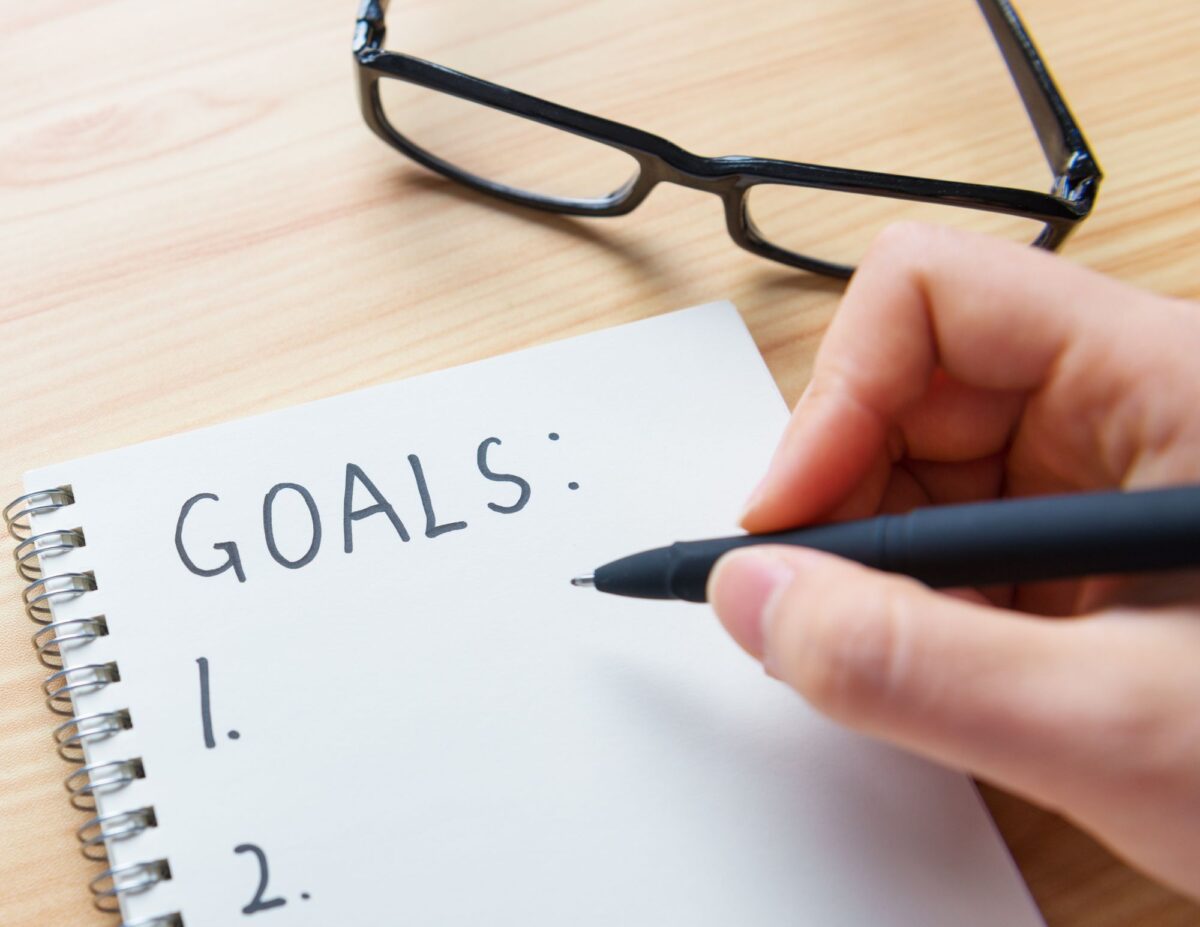 Someone is writing on a paper that says, "Goals: 1. 2." - how to declutter your home fast.