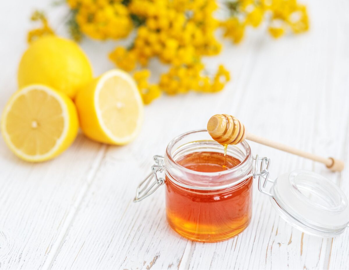 A jar of honey with a honey dipper on top with cut up lemons - frugal and natural skincare routine.