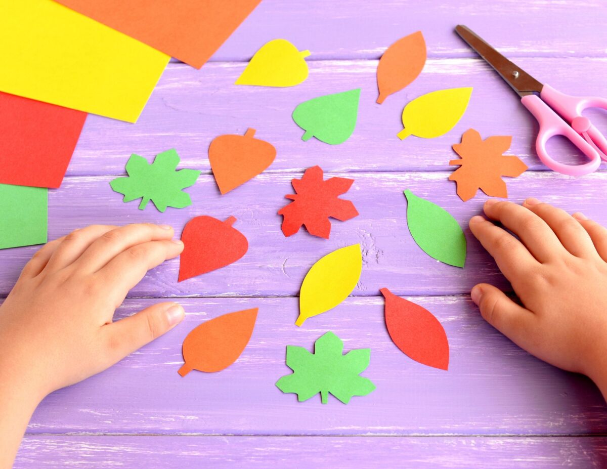 Someone's hands are on a table with brightly colored paper leaves - budget-friendly fall activities.