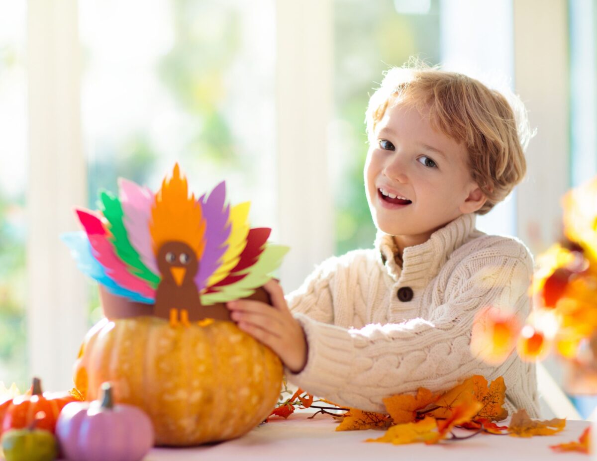 A little boy is holding a turkey that he made with paper and a pumpkin - budget-friendly fall activities.
