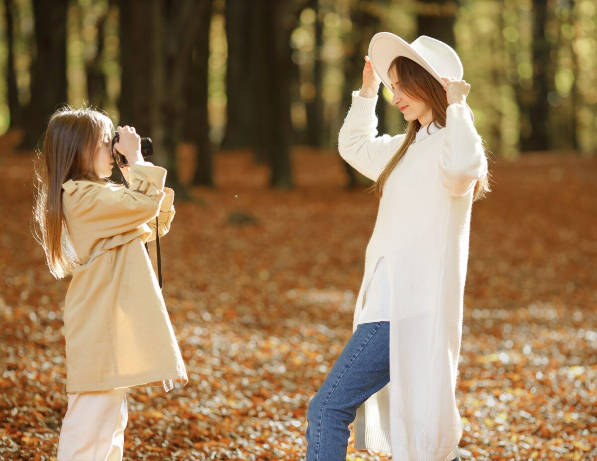 A girl is taking a picture of her mom outside with fall foliage in the background - budget-friendly fall activities