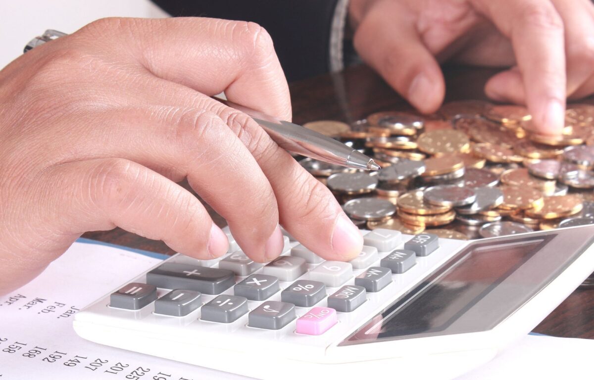 A person is counting money while using a calculator - Frugalnook category Money Management.