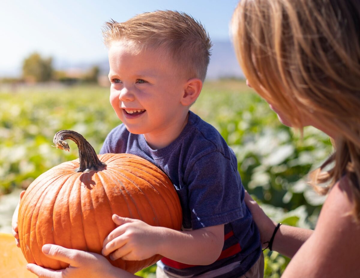 a little boy is holding a pumpkin with his mom standing next to him - budget-friendly fall activities
