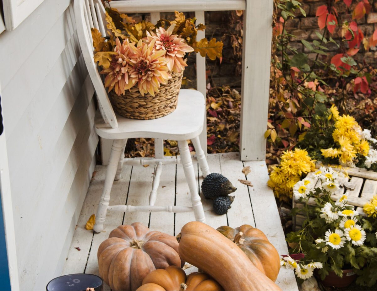 a chair on a porch with fall flowers and assorted gourds - cheap outside DIY fall decorations.