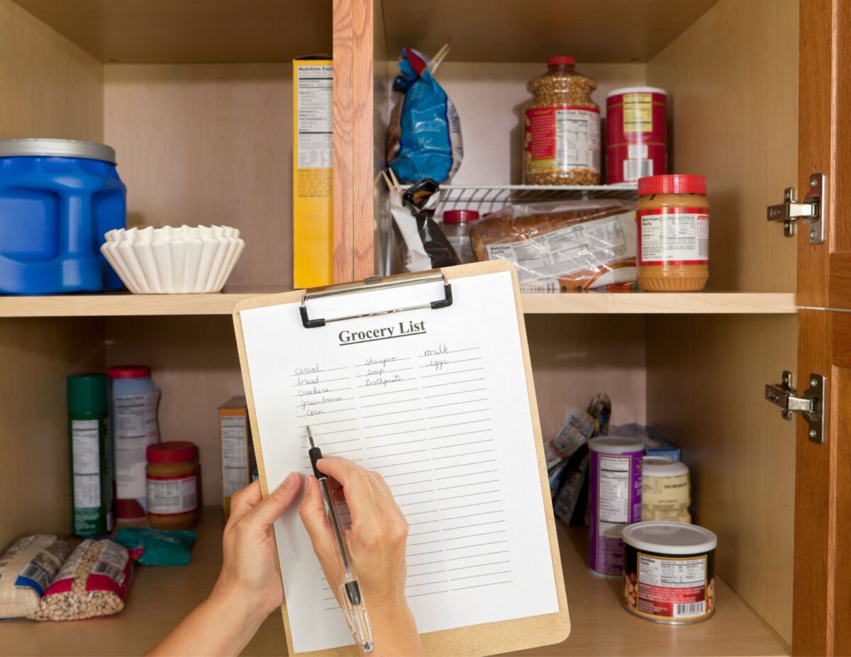 Someone is making a grocery list as they are looking into a pantry - frugal living tips for families.