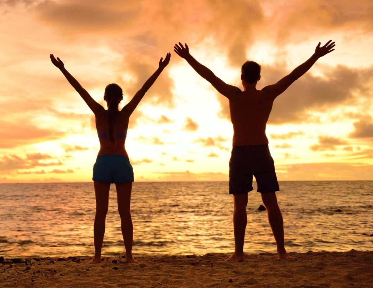Two people have their hands up in the air at the beach at dusk or sunrise - frugal living tips for families.