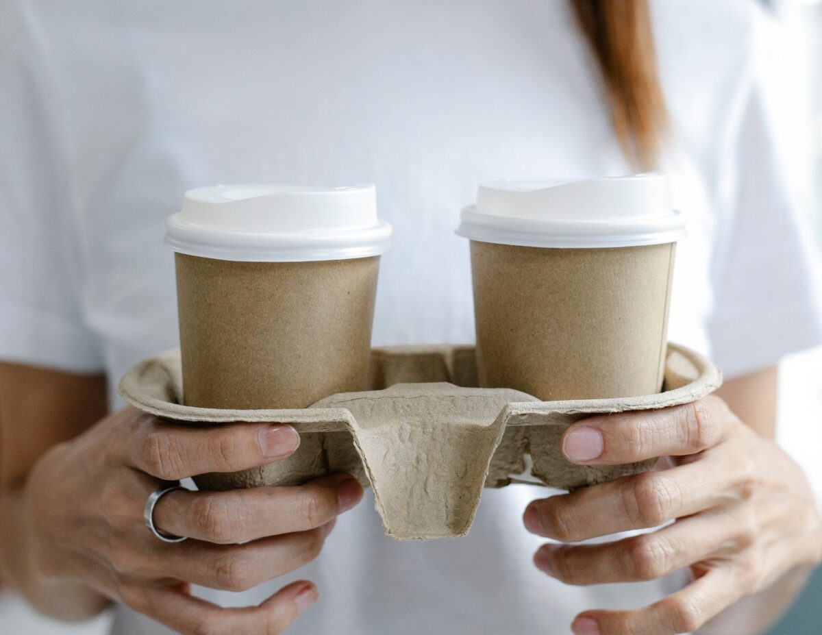 Someone is carrying two cups of coffee in a take out tray - frugal living tips for families.