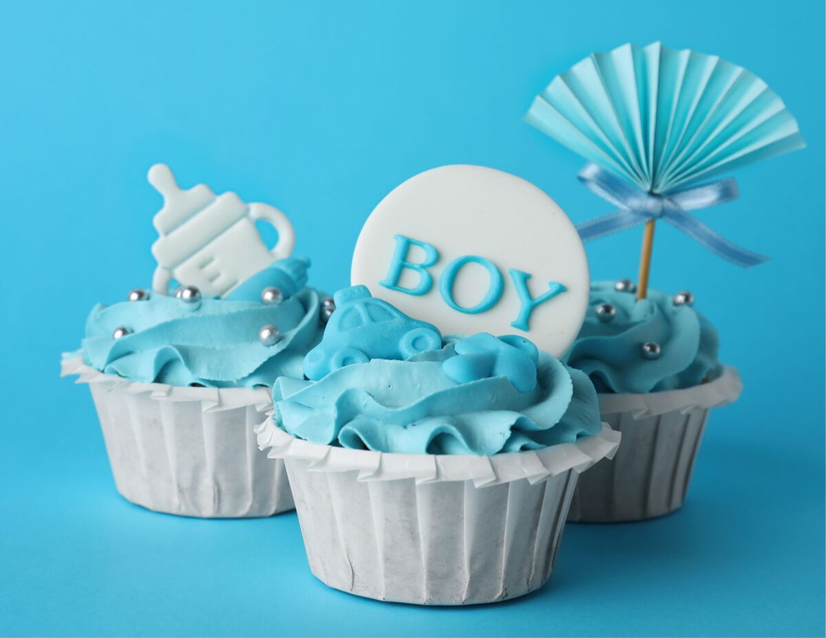 cup cakes with blue icing and topped with blue decorations and one says "boy" - cheap baby shower food ideas.