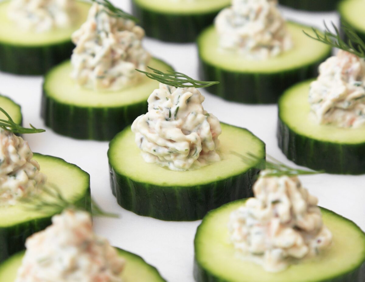 cucumber slices with dip on top, garnished with rosemary - cheap baby shower food ideas.