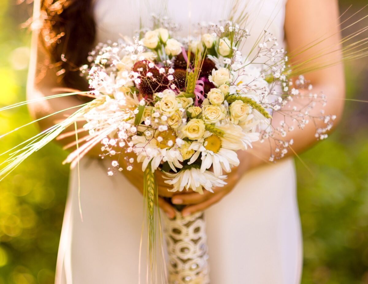 a bride is holding a bouquet of wild flowers - outdoor wedding ideas on a budget