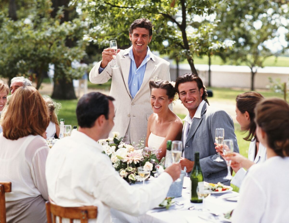 A bride and groom and guests are sitting at a table outside - outdoor wedding ideas on a budget