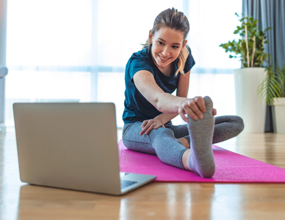 a woman doing exercises while looking at a laptop- cheap self-care ideas